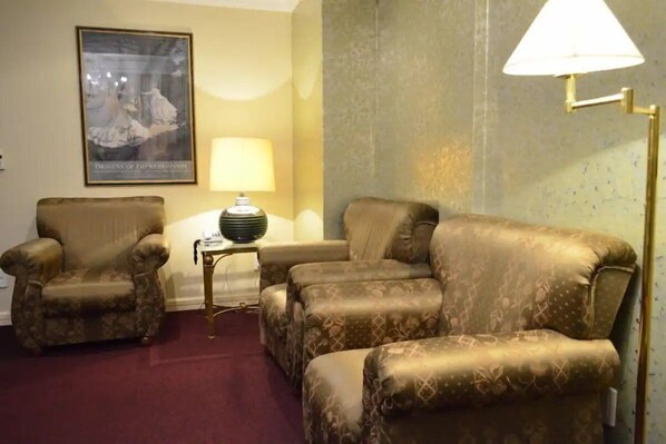 Een kamer met een gestreept bankje, twee fauteuils, een klein bijzettafeltje met een lamp en een ingelijst kunstwerk aan de muur.