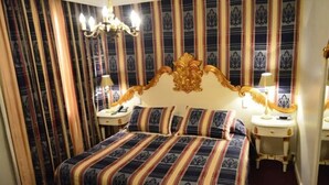 Ein Hotelzimmer mit einem großen Bett, einem verzierten Kopfteil, zwei Nachttischen mit Lampen und gestreiften Vorhängen.