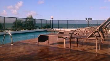 A poolside area with lounge chairs and a view of the ocean.