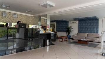 A hotel lobby with a reception desk, a sofa, a coffee table, and a clock on the wall.