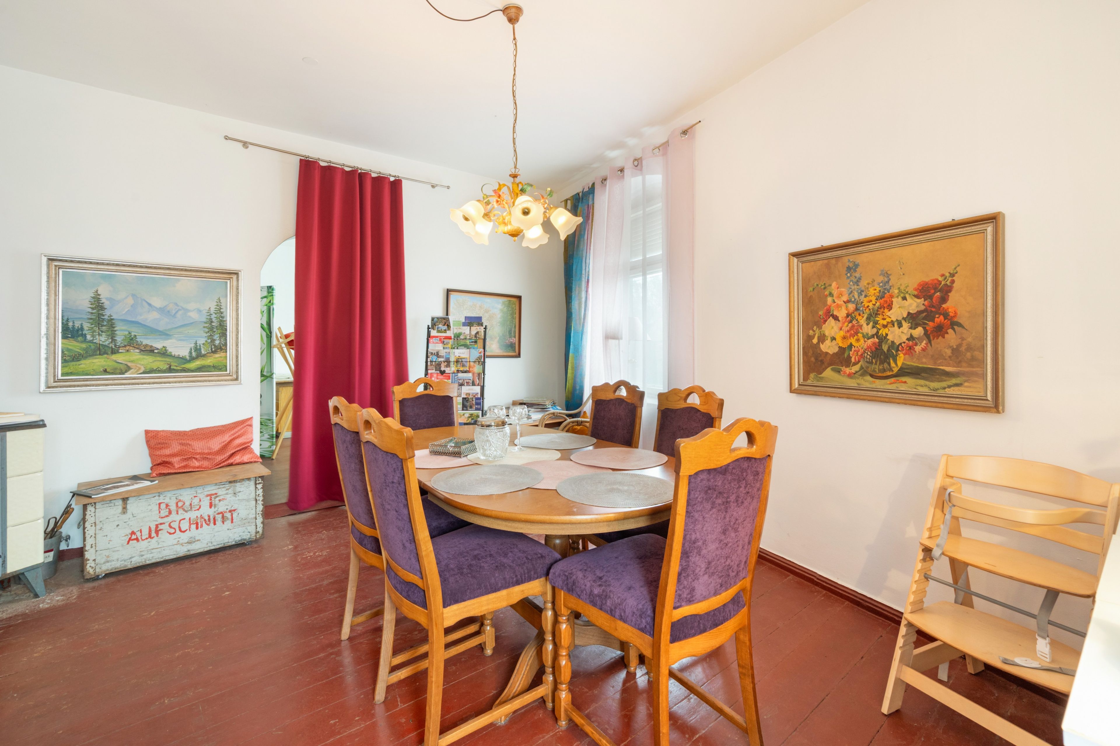 A dining area with a round table, wooden chairs, and a red curtain.