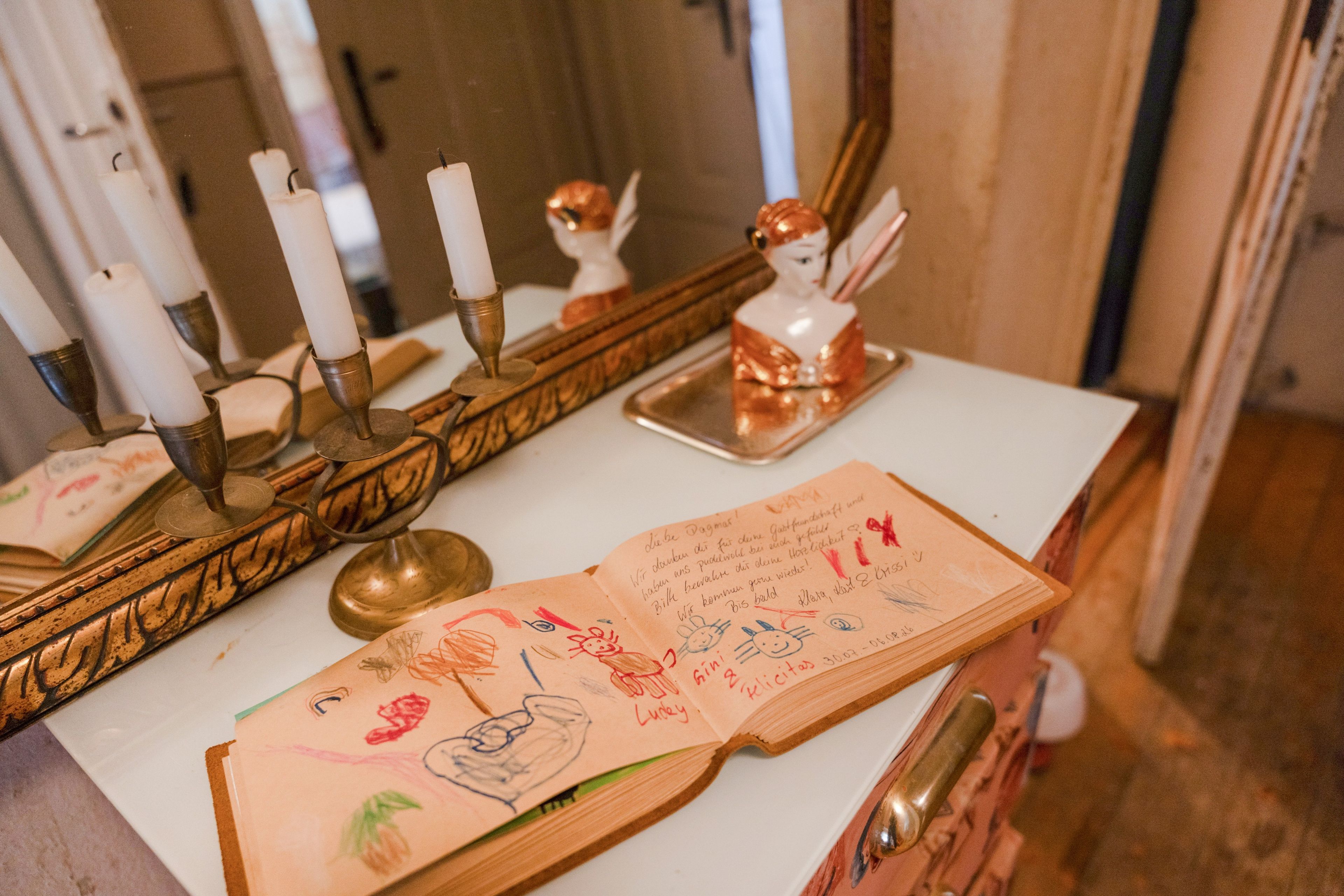 Una habitación con una mesa blanca, un espejo y un candelabro con velas. Hay un libro con notas manuscritas sobre la mesa.