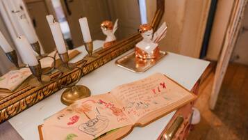 Una habitación con una mesa blanca, un espejo y un candelabro con velas. Hay un libro con notas manuscritas sobre la mesa.