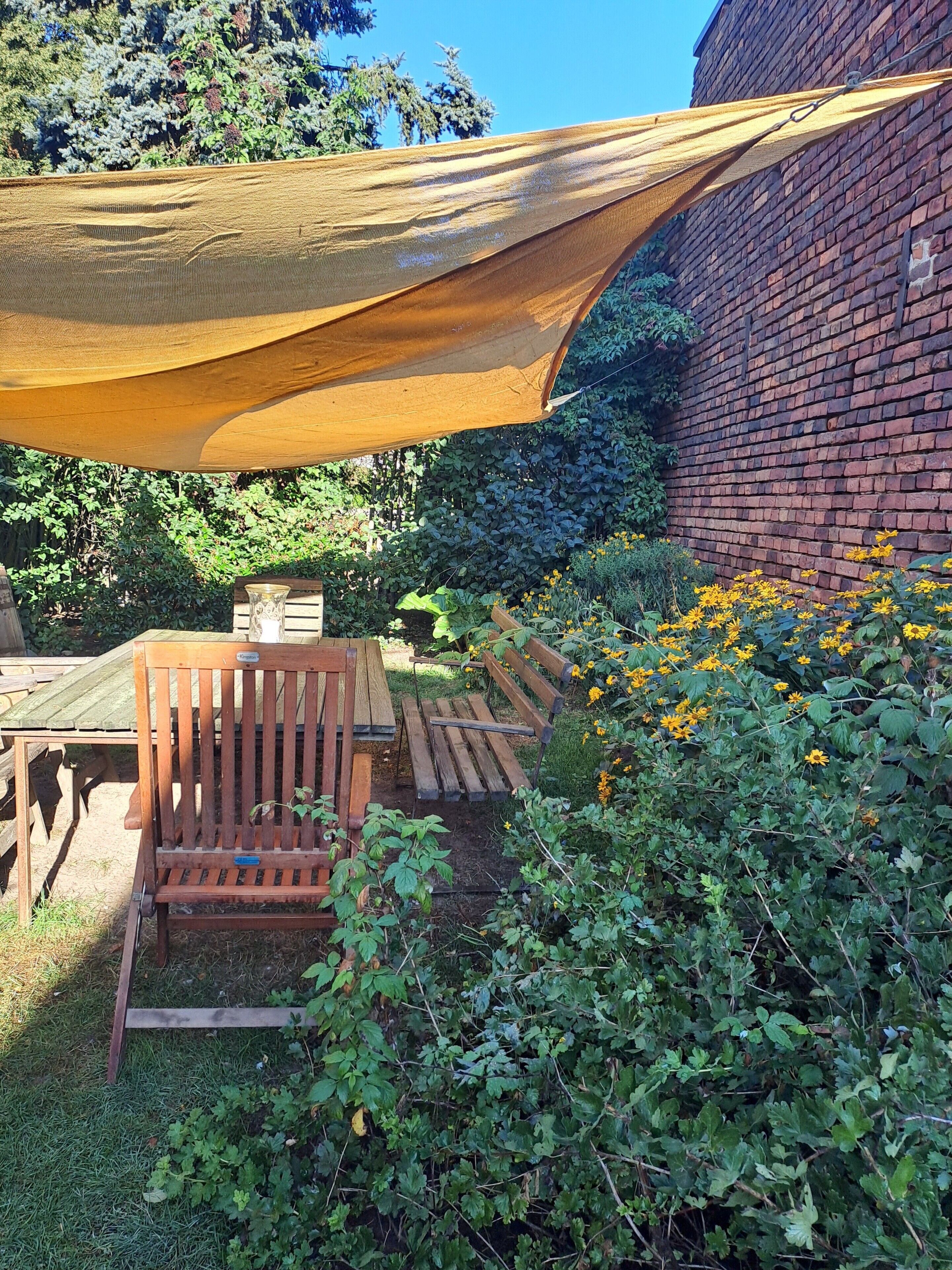 A garden area with a wooden bench, a brick wall, and a yellow shade sail.
