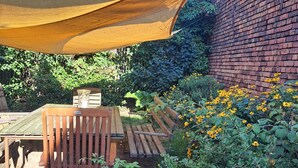 Ein Gartenbereich mit einer Holzbank, einer Ziegelwand und einem gelben Sonnensegel.