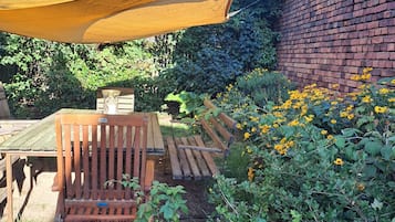 A garden area with a wooden bench, a brick wall, and a yellow shade sail.