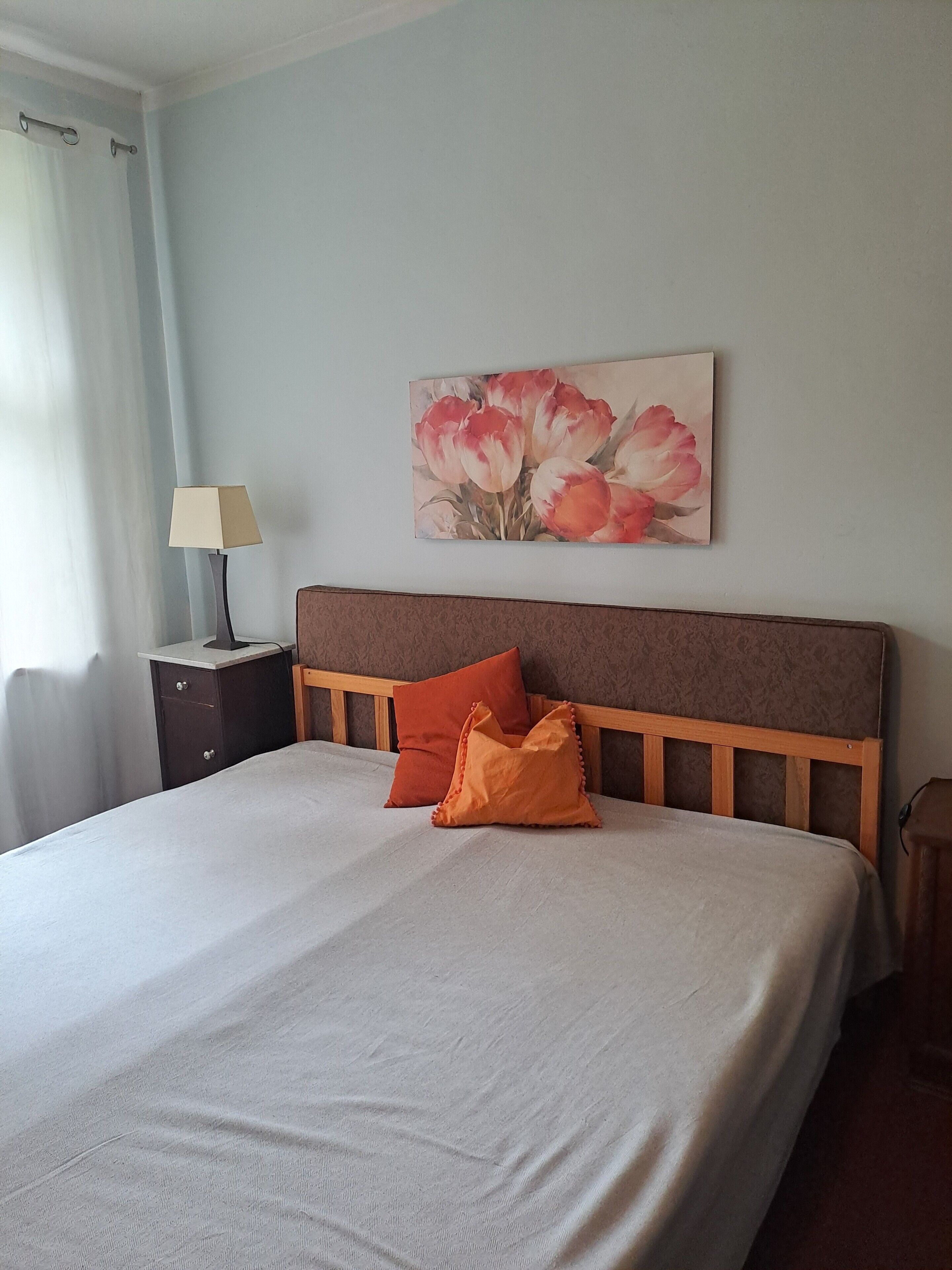 A bedroom with a bed, a nightstand, a lamp, and a painting on the wall.
