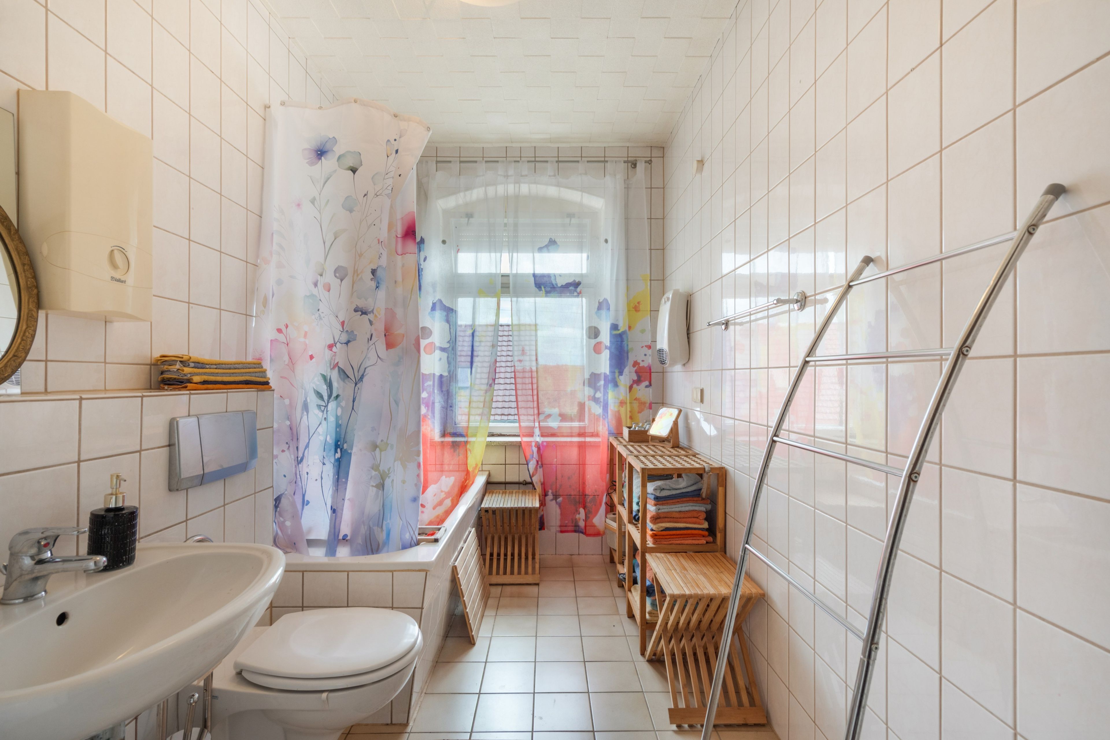 A bathroom with a toilet, sink, shower, and a wooden shelf with towels.