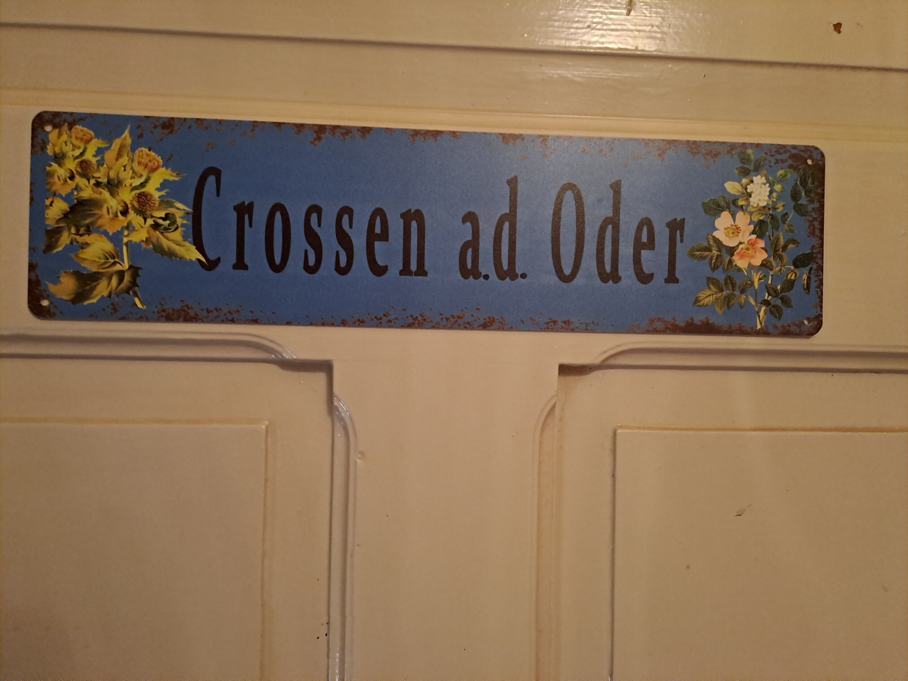 A sign with the text 'Crossen ad Oder' and floral decorations on a door.
