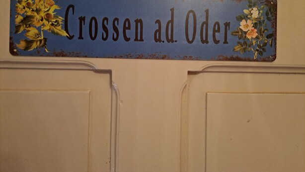 Ein Schild mit dem Schriftzug 'Crossen ad Oder' und floralen Verzierungen an einer Tür.