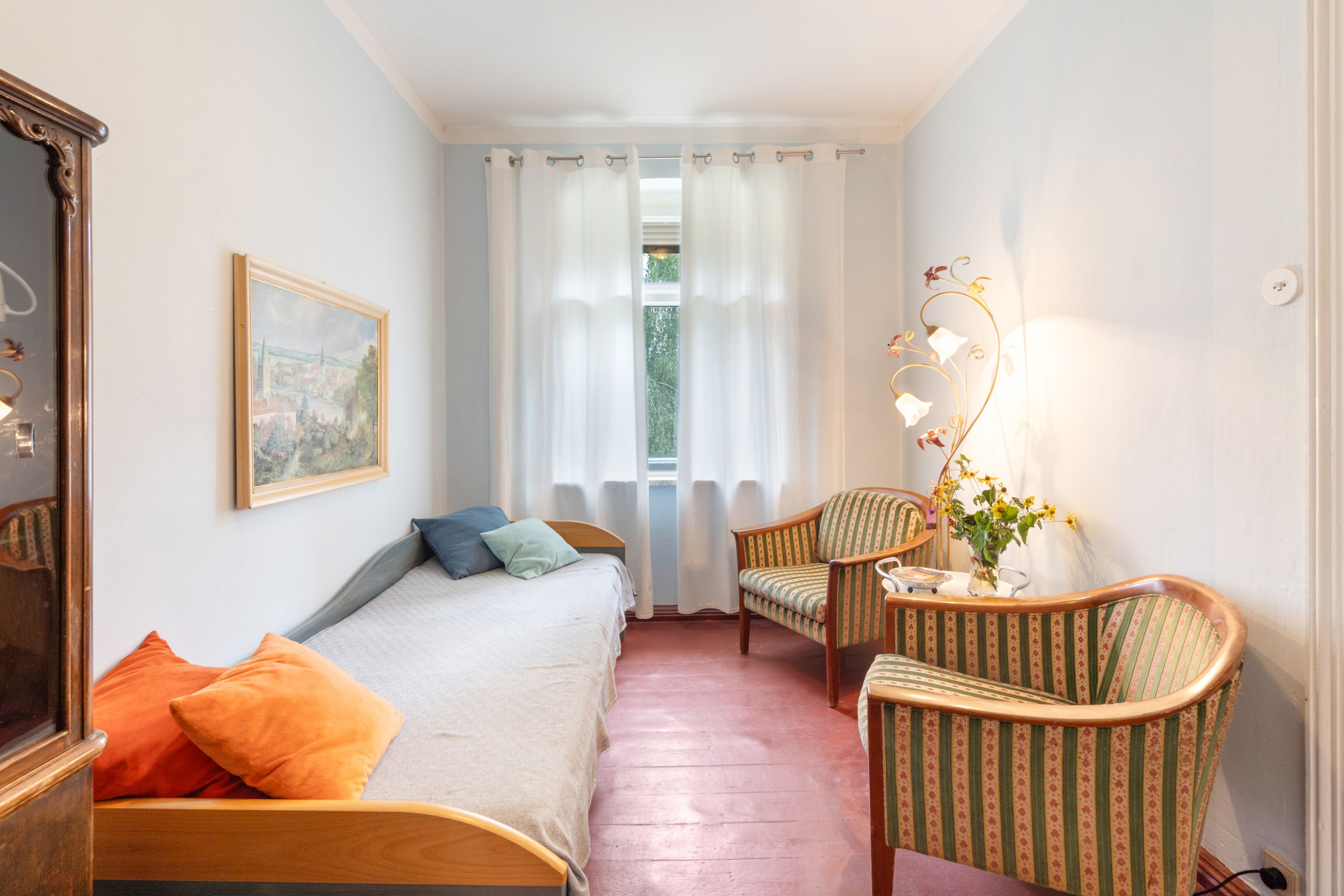 Une chambre à coucher avec un lit, une chaise, une table, une lampe et un tableau accroché au mur.