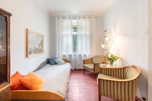 A bedroom with a bed, a chair, a table, a lamp, and a painting on the wall.