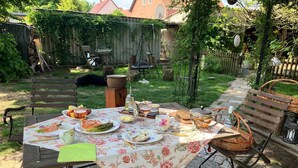 An outdoor dining area with a table set for a meal, surrounded by a garden and a wooden fence. - Apartment ',,Dresden Hellerau,,' with Shared Terrace, Private Garden and Wi-Fi (Forst (Lausitz))