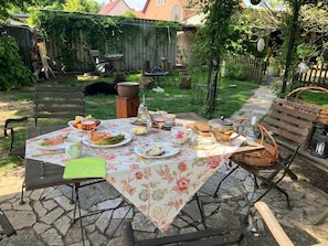 Een buiten eethoek met een gedekte tafel, omgeven door een tuin en een houten schutting.
