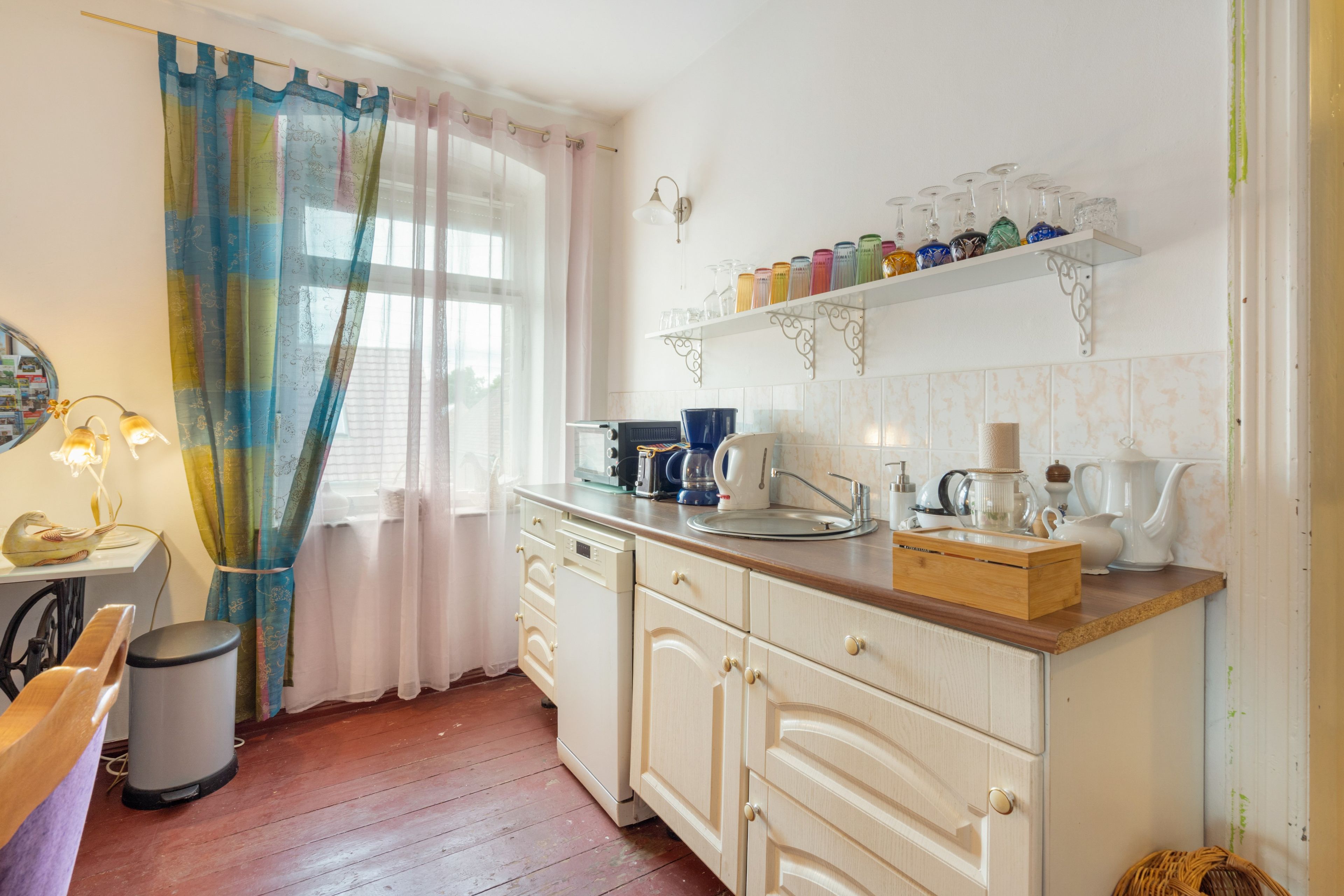 Una cocina con muebles de madera, encimera, lavamanos y una ventana con cortinas.