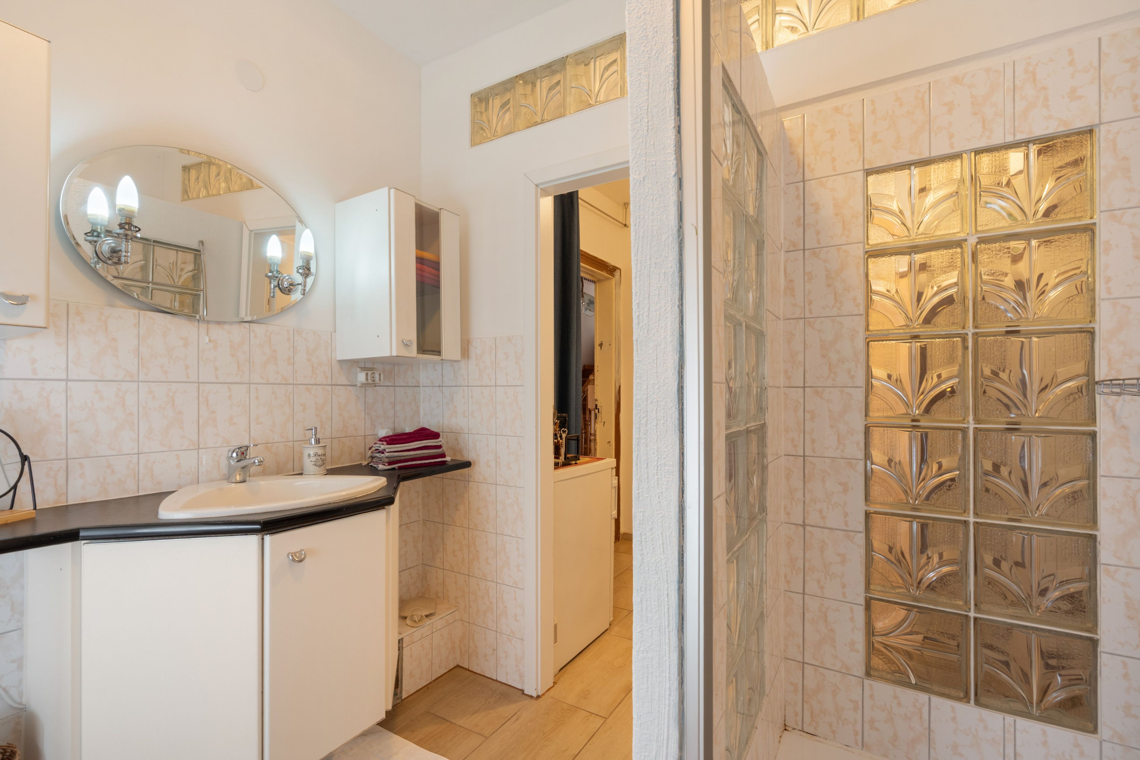 A bathroom with a sink, mirror, cabinet, and a shower area with decorative glass panels.