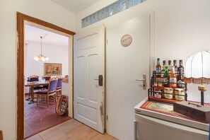 A room with a dining area, a door with a 'Bathroom' sign, and a shelf with various bottles and jars.