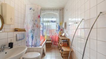 A bathroom with a toilet, sink, shower, and a wooden shelf with towels.