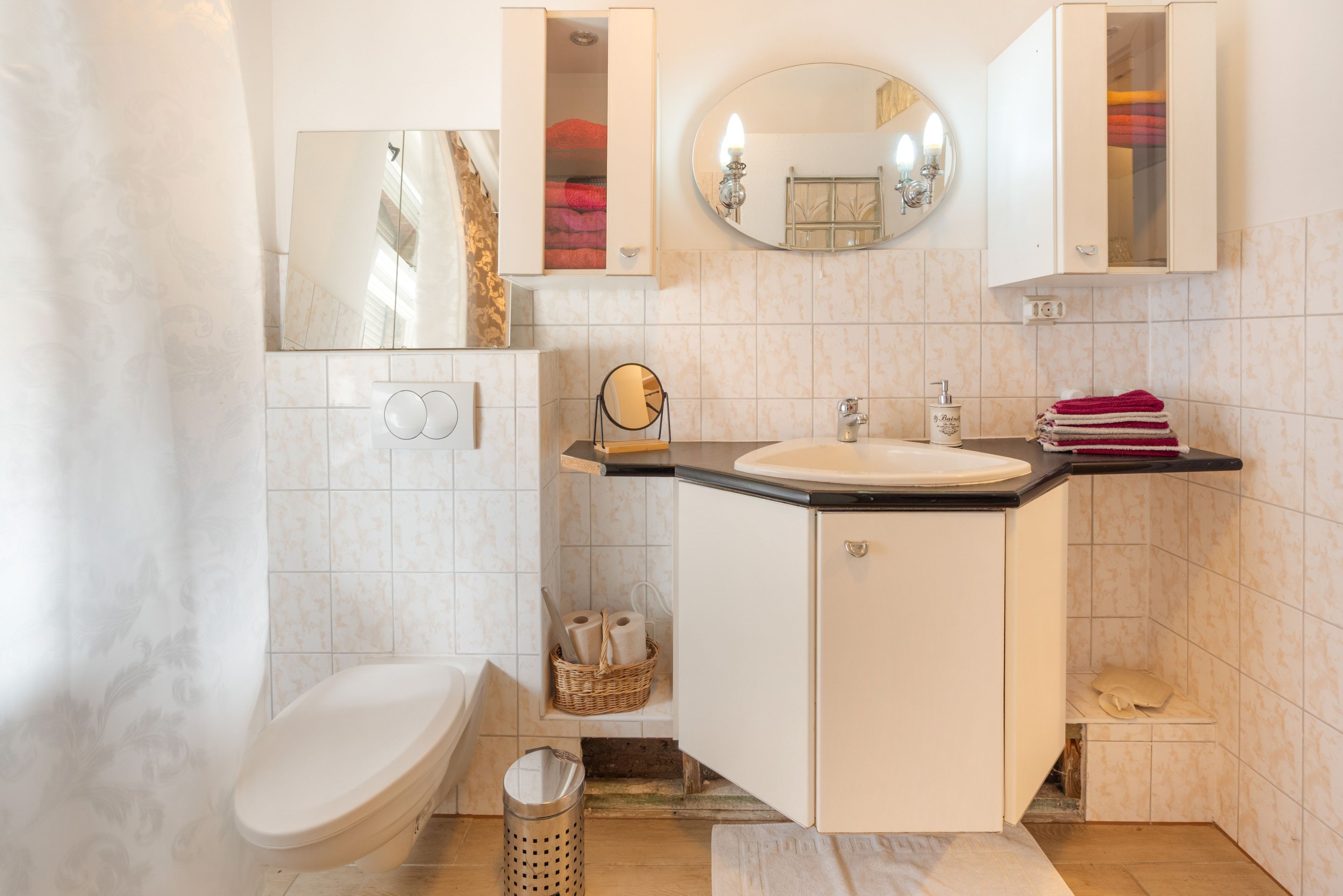 A bathroom with a toilet, sink, mirror, and storage cabinets.