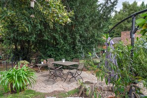 A patio area with a table and chairs, surrounded by greenery and trees.