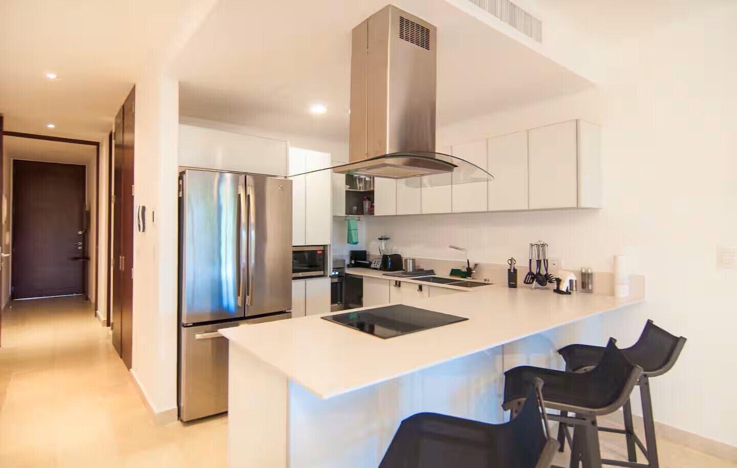 A modern kitchen with a stainless steel refrigerator, a built-in oven, and a large island with bar stools.
