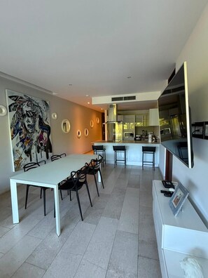 A modern kitchen with stainless steel appliances, a dining area with a white table and black chairs, and a large abstract painting on the wall. - Cozy apartment with a Jacuzzi and beautiful views (Playa del Carmen)