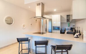 A modern kitchen with a central island, bar stools, a stainless steel range hood, and built-in appliances. - Cozy apartment with a Jacuzzi and beautiful views (Playa del Carmen)