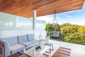 A modern outdoor seating area with a sofa, a hanging chair, and a coffee table with a plant. - Cozy apartment with a Jacuzzi and beautiful views (Playa del Carmen)