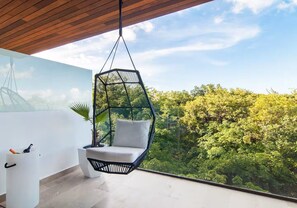 A hanging chair with a cushion, a white storage unit, and a view of a lush green landscape. - Cozy apartment with a Jacuzzi and beautiful views (Playa del Carmen)