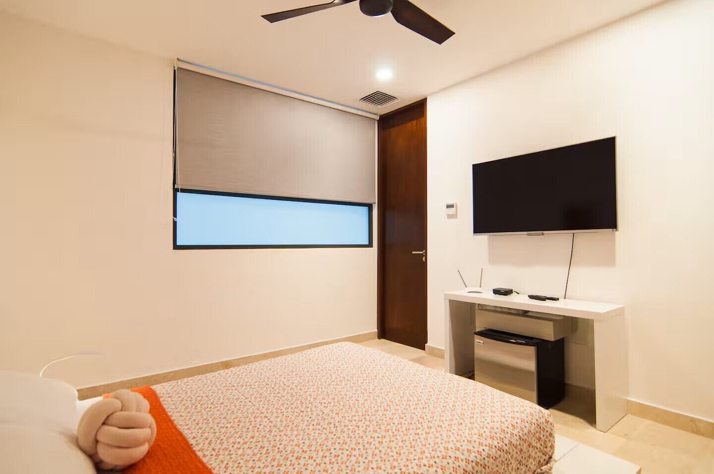 A hotel room with a bed, a desk with a flat-screen TV, a ceiling fan, and a window with a view.