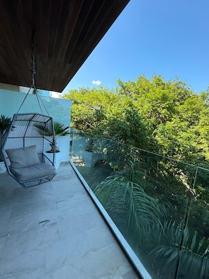 Een balkon met een hangstoel, glazen balustrade en weelderige beplanting.