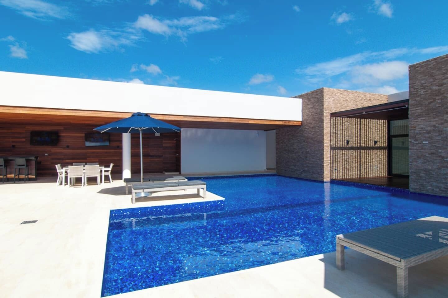 A modern outdoor pool area with lounge chairs, a table, and an umbrella.