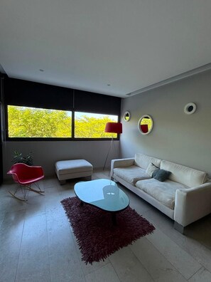 A modern living room with a sofa, a red chair, a glass coffee table, and a red rug. - Cozy apartment with a Jacuzzi and beautiful views (Playa del Carmen)