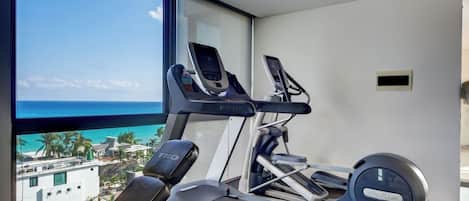 Une salle de sport équipée de tapis de course et d’un vélo d’appartement, une fenêtre donnant sur l’océan et une bouche d’aération au plafond.