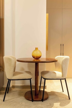 Een ronde houten tafel met een gele vaas, omringd door twee gestoffeerde stoelen met een geribbelde stof.