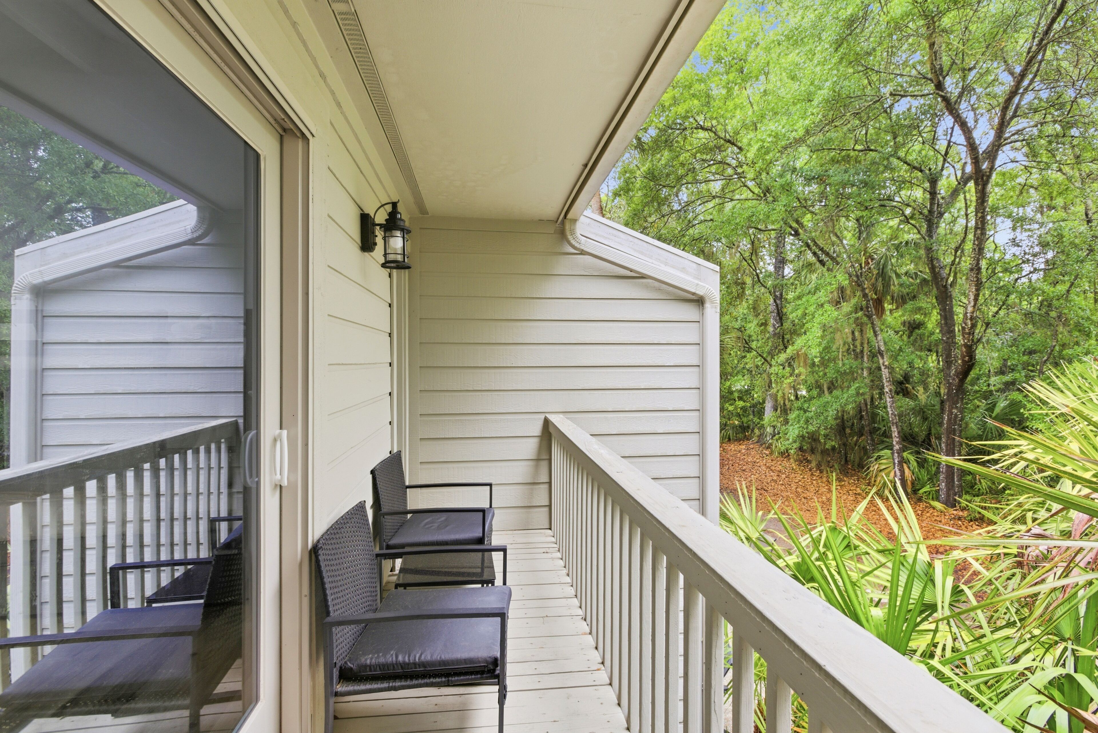 A covered porch with two chairs and a table, overlooking a garden with trees and plants.