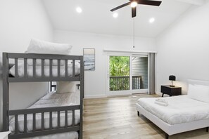 A bedroom with a bunk bed, a single bed, a ceiling fan, a nightstand, and a view of greenery through a sliding door. - Sunset Rentals | Sailmaster 46 (Hilton Head Island)