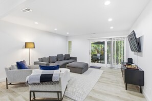 A modern living room with a sectional sofa, a small couch, a floor lamp, and a chessboard on a side table. - Sunset Rentals | Sailmaster 46 (Hilton Head Island)