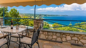 An outdoor seating area with stone walls, a table, chairs, and a view of the sea. - Koroni Akrita Residence, Venetico Seafront Charm (Koroni)