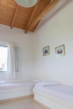 Une pièce avec un plafond en bois, deux lits, une fenêtre avec des rideaux et deux tableaux encadrés accrochés au mur.