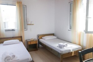 Une chambre d’hôtel avec deux lits simples, une table de chevet avec une lampe et une fenêtre avec des rideaux.