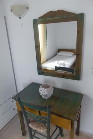 Ein kleines Zimmer mit einem Einzelbett, einem Holztisch mit einem gewebten Korb und einem Spiegel an der Wand.