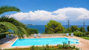 A swimming pool with lounge chairs, a stone wall, and a view of the sea. - Koroni Akrita Residence, Venetico Seafront Charm (Koroni)