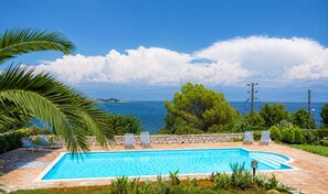 Une piscine avec des chaises longues, un mur en pierre et une vue sur la mer.