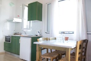 Une cuisine compacte avec des meubles de couleur verte, un réfrigérateur blanc et une table à manger avec des chaises.