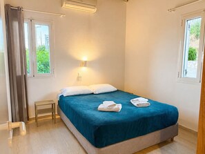 Une chambre à coucher avec un lit, une table de chevet, une lampe fixée au mur et une fenêtre avec des rideaux.