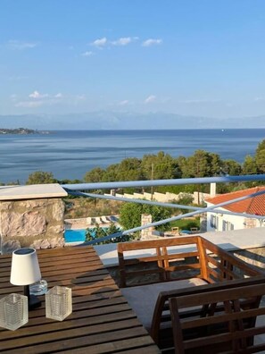 Une terrasse en bois avec une table et des chaises, offrant une vue sur une étendue d’eau et un paysage montagneux.