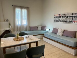 Een compacte leefruimte met een slaapbank, een eettafel met stoelen en een wandlamp.