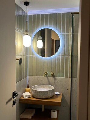 Une salle de bain avec un miroir rond, un lavabo en pierre et un porte-serviettes.