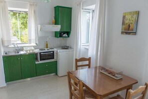 Een kleine keuken met groene kastjes, een wit aanrecht, een oven, een koelkast en een eettafel met stoelen.